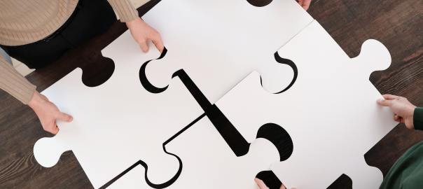 Neljä ihmistä sovittamassa neljää palapelin palaa yhteen kuvattuna ylhäältä päin.