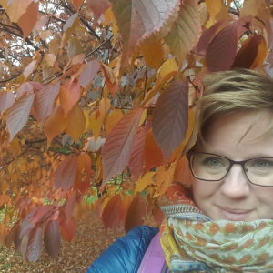 Silmälasipäinen nainen on syksyisten puunlehtien lähellä.