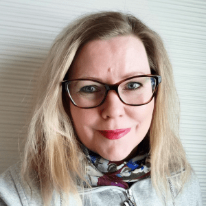 Lähikuva silmälasipäisestä, vaaleahiuksisesta naisesta.