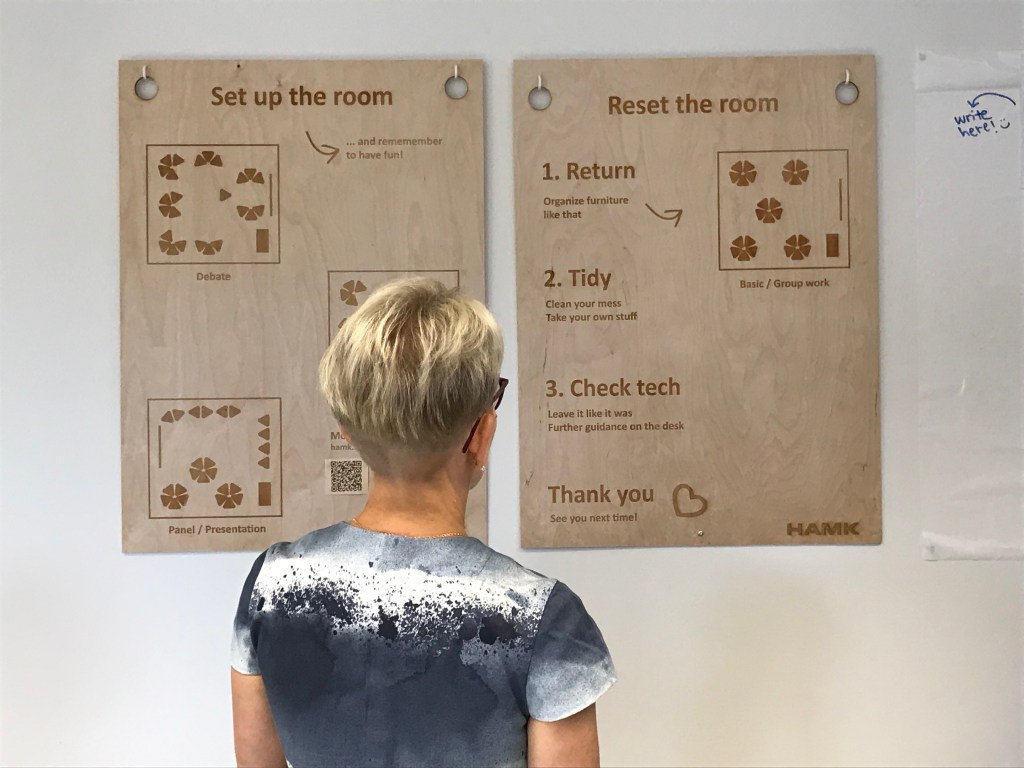 Takaapäin kuvattu nainen katsomassa ohjeita, miten pöytiä on mahdollista järjestellä luokkahuoneessa.