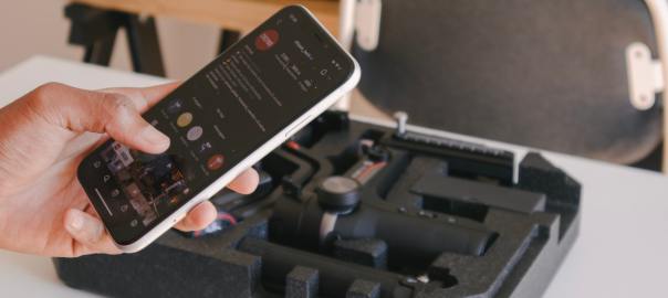 Käsi pitelee puhlinta. Taustalla gimbaali paketissa.